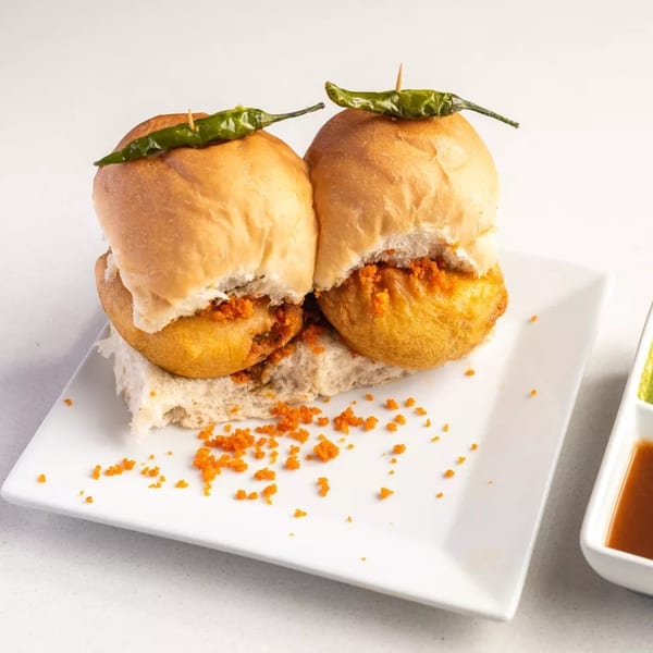 Two vada pav sliders with green chilies on top, served with green and brown chutneys.