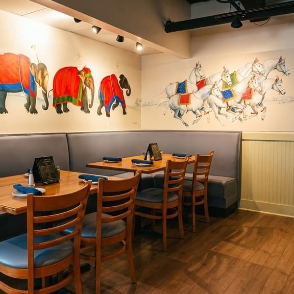 Restaurant interior with elephant and horse murals, booth seating, wooden tables, and chairs.