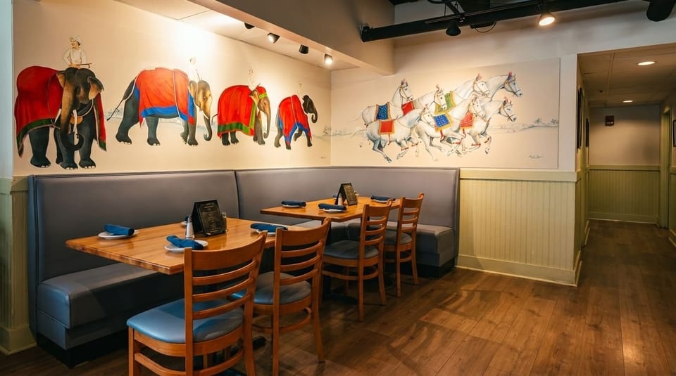 Restaurant interior with elephant and horse murals, booth seating, wooden tables, and chairs.