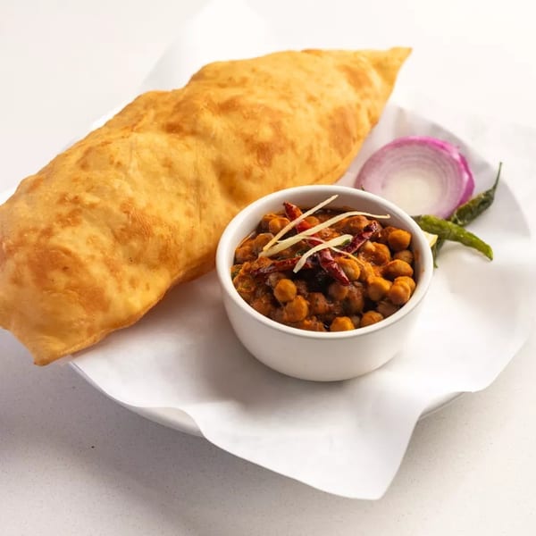 A golden fried flatbread (puri) served with a bowl of chickpea curry (chole) and sliced onions.
