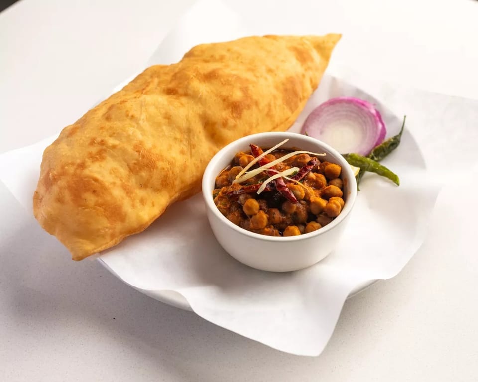 A golden fried flatbread (puri) served with a bowl of chickpea curry (chole) and sliced onions.