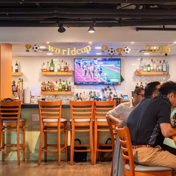 Patrons seated at a bar with a "Worldcup 2026" banner and a TV showing a track event.