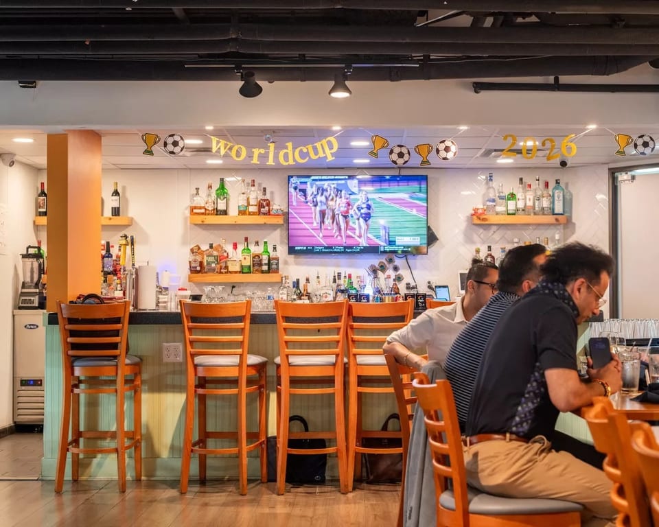 Patrons seated at a bar with a "Worldcup 2026" banner and a TV showing a track event.