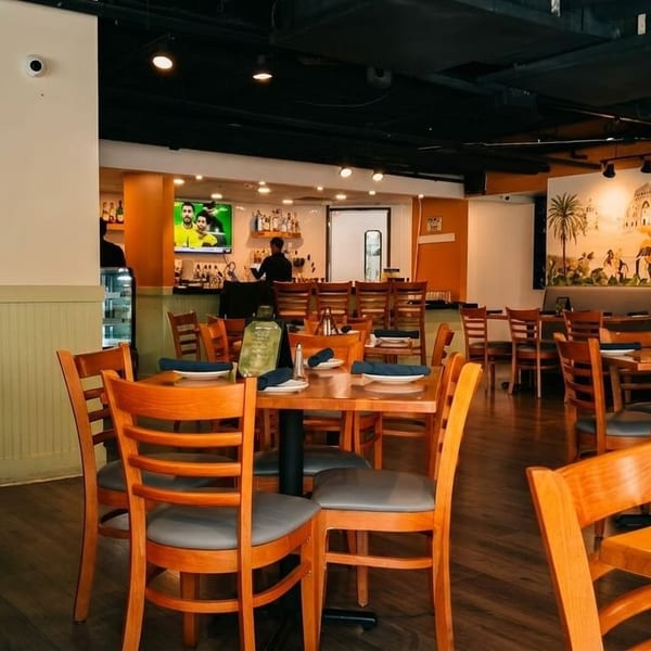Empty restaurant dining room with wooden tables and chairs, a bar, and a large mural on the wall.