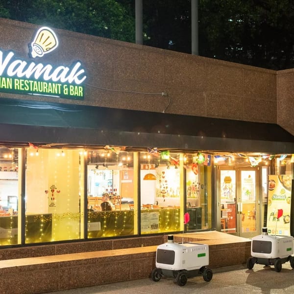 Exterior of Namak Indian Restaurant & Bar at night with two delivery robots outside.