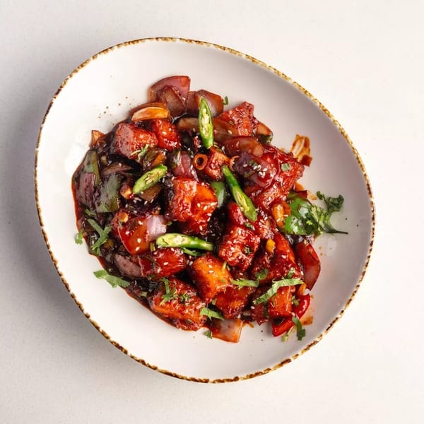 Chili Paneer with red sauce, green chilies, onions, and cilantro in a white bowl.