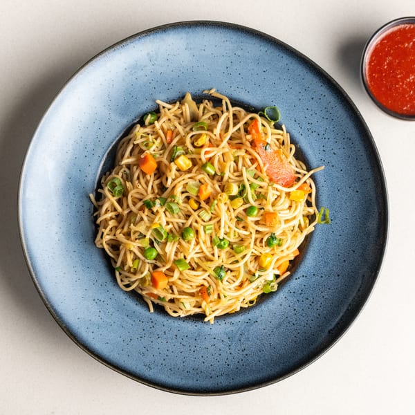 Vegetable chow mein noodles with carrots, peas, corn, and bell peppers, served with red sauce.