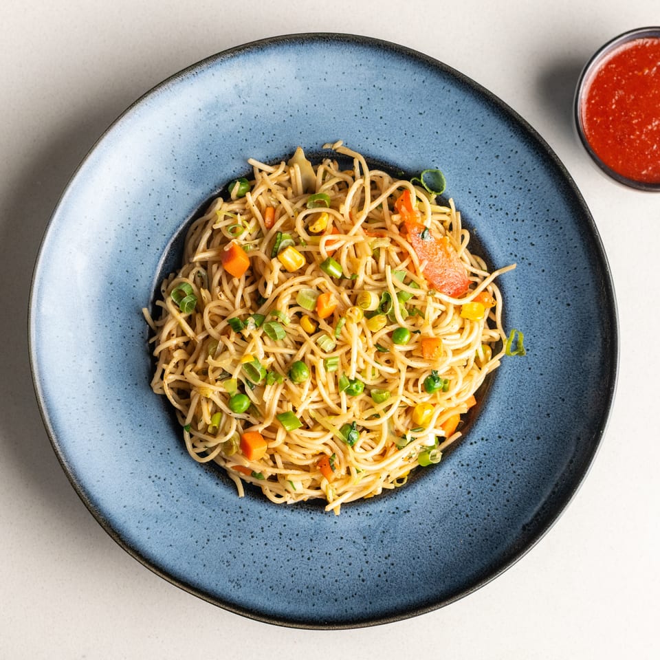 Vegetable chow mein noodles with carrots, peas, corn, and bell peppers, served with red sauce.