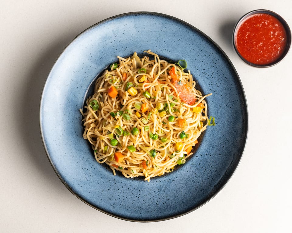 Vegetable chow mein noodles with carrots, peas, corn, and bell peppers, served with red sauce.