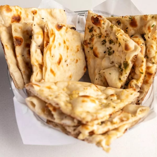 A basket filled with various types of naan bread, including plain, garlic, and herb.