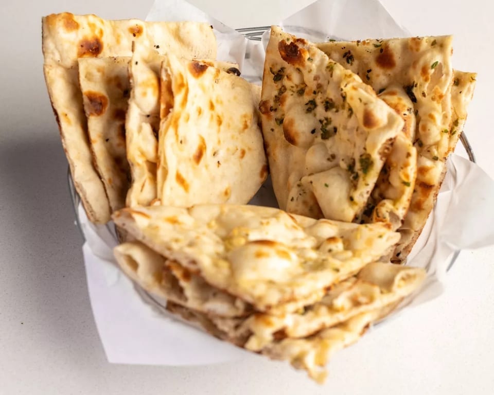 A basket filled with various types of naan bread, including plain, garlic, and herb.