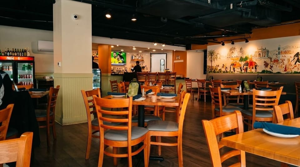 An empty restaurant dining room with wooden tables and chairs, a bar, and a mural on the wall.